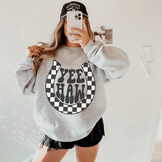 Long sleeve, oversize Gildan crewneck sweatshirt in Sport Grey with a black and white checker print horseshoe featuring the words Yee Haw in the centre.
