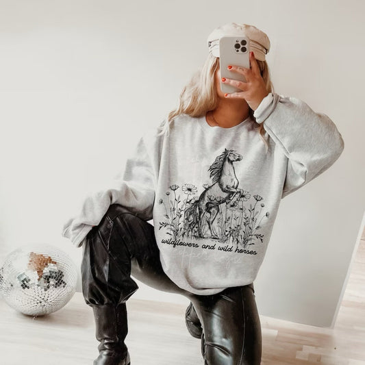 Oversized crewneck sweatshirt in grey featuring a graphic of a wild horse in a field of wildflowers with the lyrics &quot;Wildflowers and Wild Horses&quot;